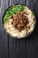 Recipe forÂ dan dan noodlesÂ with minced meat and greens closeup in a plate. Vertical top view